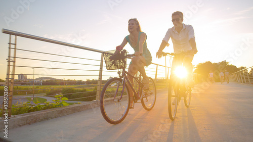 LENS FLARE Young woman smiles while riding a bike with her boyfriend at sunrise