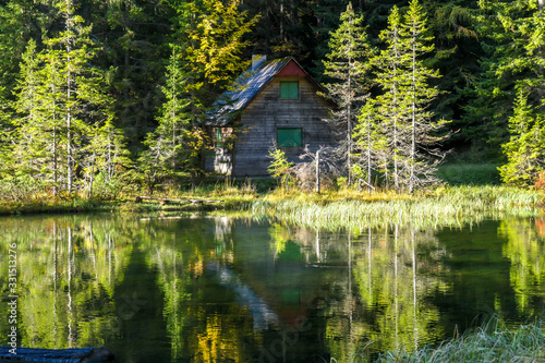 A small cottage at the side of alpine Joser Lake  located between the woods  next to a pathway leading to Buchbergkogel  Austria. Calm surface of the lake with many reflections. Forged perspective