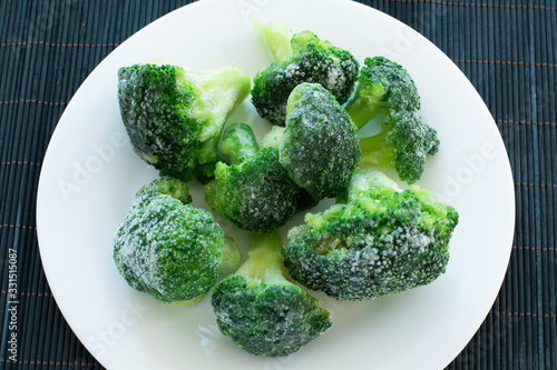 frozen green broccoli on the white plate and black bamboo wood background