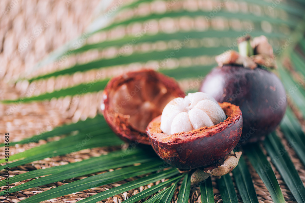 Mangosteen with palm leaves on rattan background. Copy space. Tropical travel, exotic fruit. Vegan and vegetarian concept Mangosteen with palm leaves on rattan background. Copy space. Tropical travel, exotic fruit. Vegan and vegetarian concept