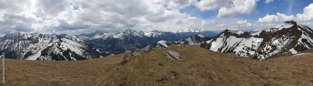 A panoramic view from top of Himmeleck in Austrian Alps. There is a massive mountain range in the back, partially covered with snow. Early spring vibes. barren mountain slopes. Overcast. Achievement