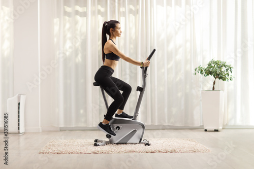 Billede på lærred Young woman exercising on a stationary bike at home