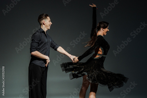 elegant young couple of ballroom dancers in black outfits dancing in dark