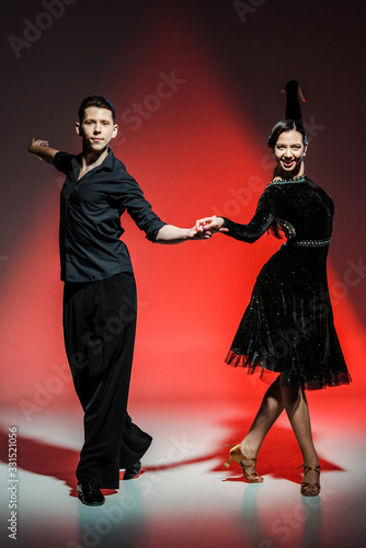 elegant young couple of ballroom dancers in black outfits dancing in red light