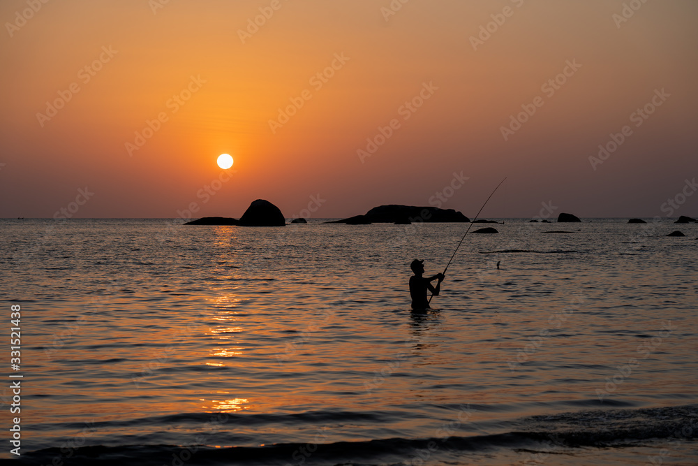 Figure of fisherman with a rod against the background of sea sunset