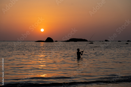 Figure of fisherman with a rod against the background of sea sunset
