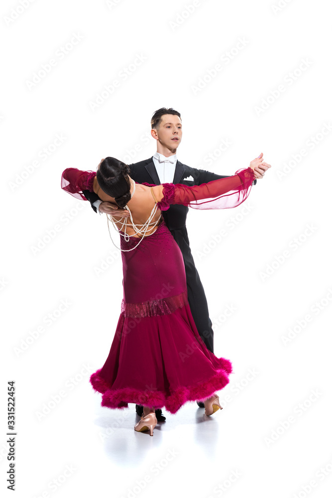 elegant young couple of ballroom dancers in red dress in suit dancing on white
