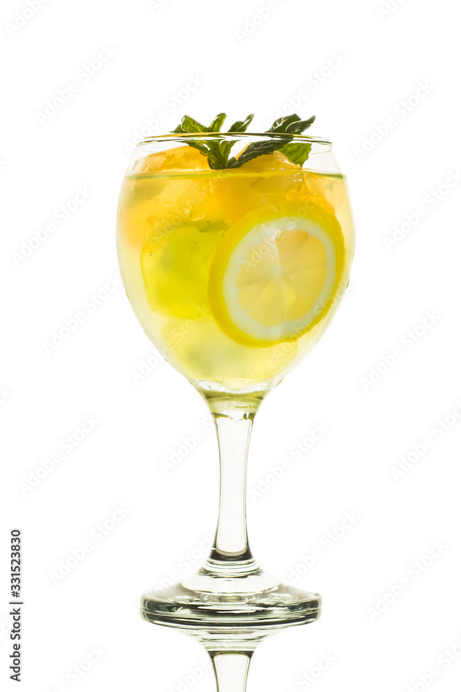 A glass of lemonade with mint and lemon slice on white background with reflection of glass. A glass of lemonade with mint and lemon slice on white background with reflection of glass.