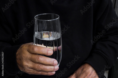 Hand of older person holding a glass of water on dark background.