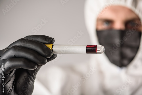 a virologist in a black mask and medical gloves wearing a white protective suit, conducts blood tests and samples for coronavirus, tests. Pandemic. Isolated and in a panic because of the epidemic. 