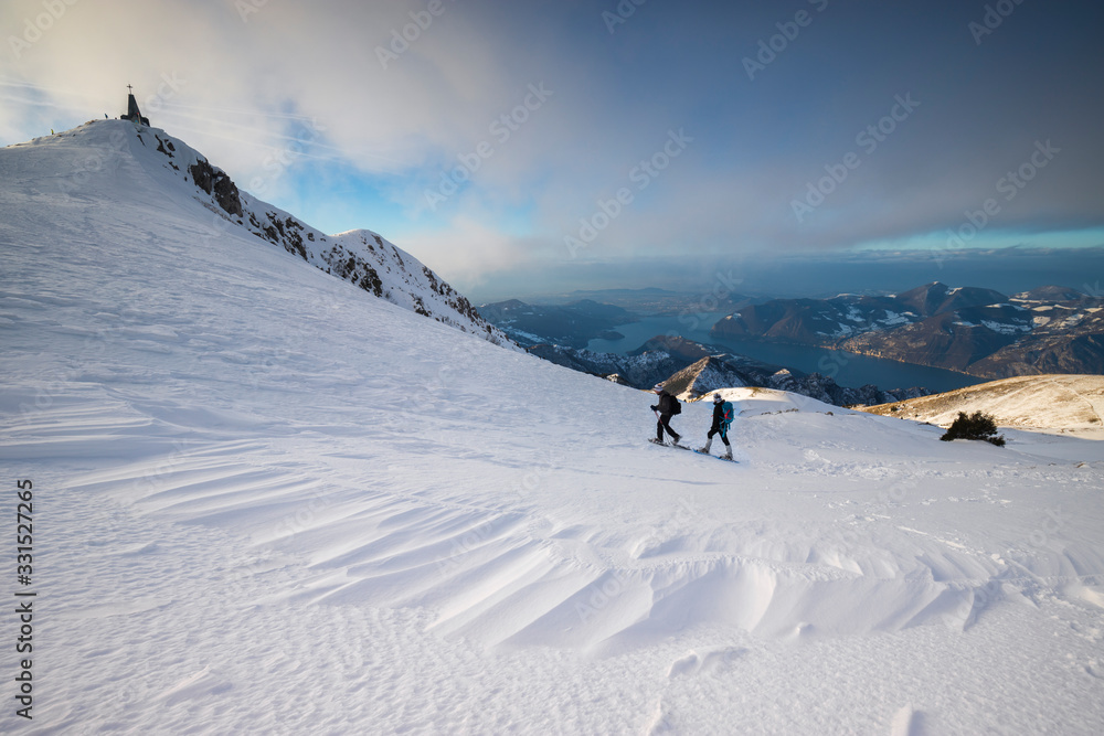 Two hikers snowshoeing on snow covered mountain peak, Brescia, Italy