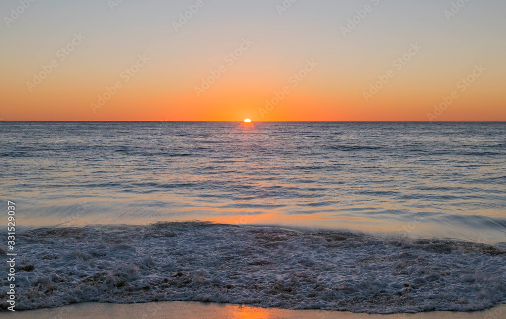 Sunset at beach in Mexico. Sun is orange and setting at horizon, blue water in foreground. Sunset at beach in Mexico. Sun is orange and setting at horizon, blue water in foreground.