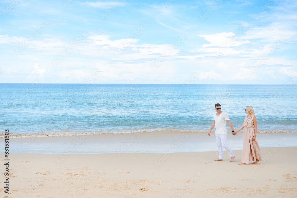 Young attractive man and woman in love walk and hug against the background of white sand and azure sea. Travel, honeymoon Young attractive man and woman in love walk and hug against the background of white sand and azure sea. Travel, honeymoon