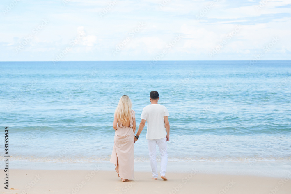 Young attractive man and woman in love walk and hug against the background of white sand and azure sea. Travel, honeymoon Young attractive man and woman in love walk and hug against the background of white sand and azure sea. Travel, honeymoon
