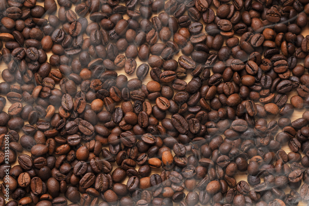 handful of hot coffee beans on wooden background with steam