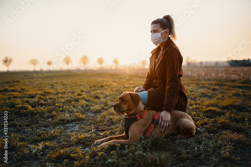 Woman wearing a protective mask is walking alone with a dog outdoors because of the corona virus pandemic covid-19 photo