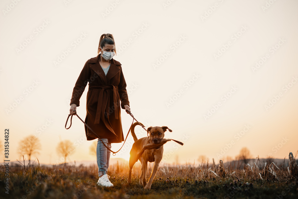 Woman wearing a protective mask is walking alone with a dog outdoors because of the corona virus pandemic covid-19