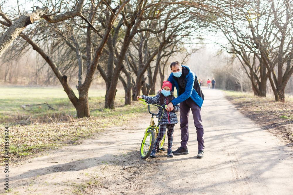 Fototapeta premium Little girl wearing medical mask prevent flu, pollutions and covid-19 riding bicycle outdoor.