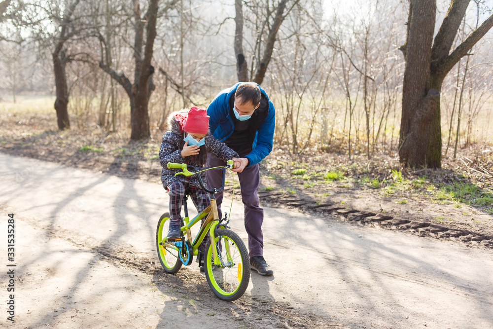 Obraz premium Caucasian father helping daughter ride bicycle wearing protection mask for protect pm2.5 and Coronavirus Covid-19 Pandemic virus symptoms.