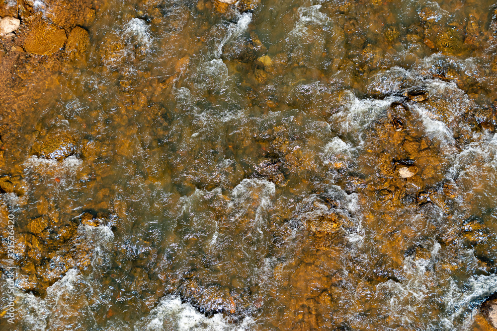 A background texture of a river flowing over brown rocks A background texture of a river flowing over brown rocks