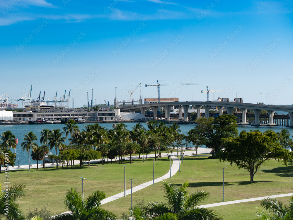 Port of Miami water front park, bridge overpass, and cranes for loading ships.
