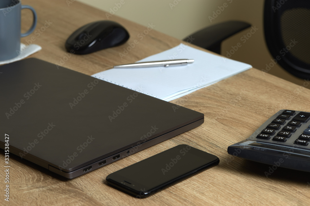 Remote work laptop calculator notepad with pen and phone on the table near chair Remote work laptop calculator notepad with pen and phone on the table near chair
