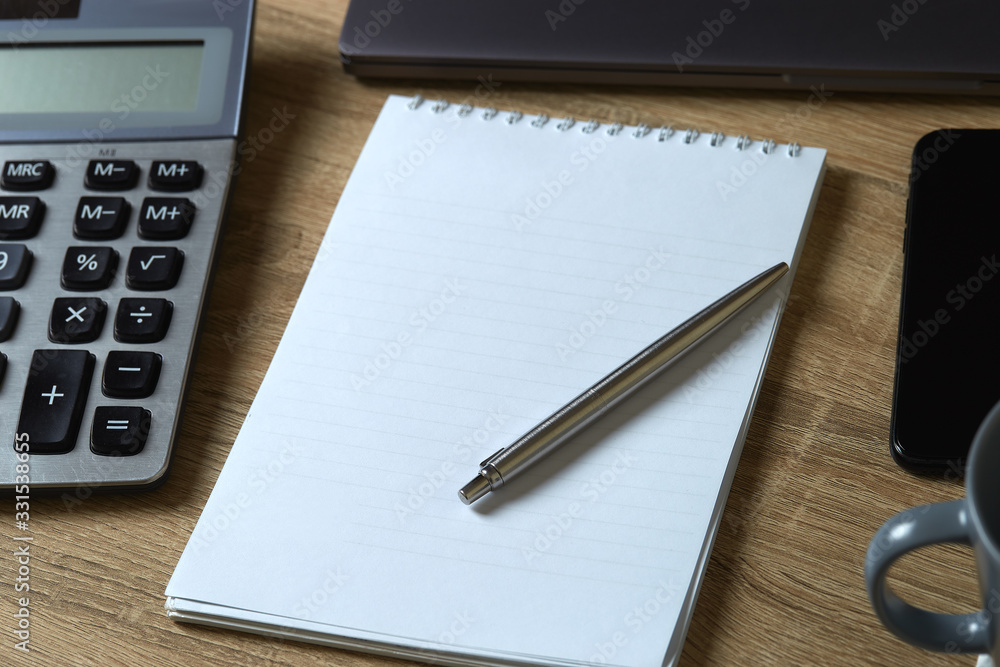 Remote work laptop calculator phone notepad with pen and part of mug on the table Remote work laptop calculator phone notepad with pen and part of mug on the table