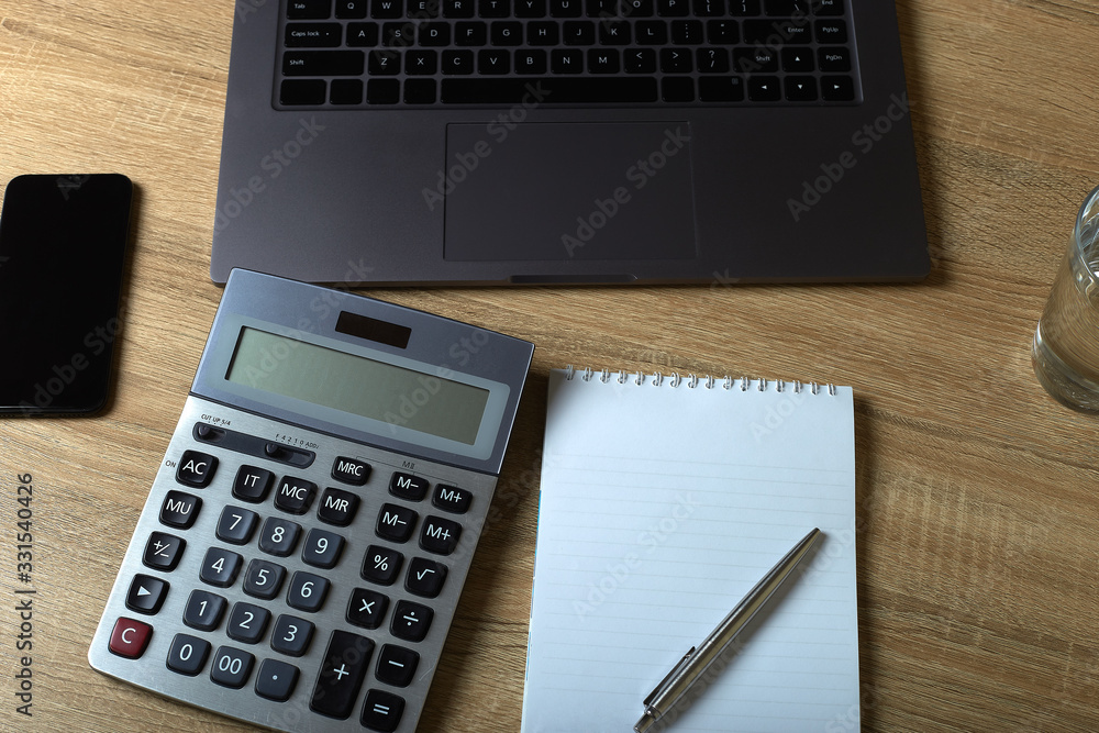 Remote work laptop calculator notepad with pen and glass of water on the table Remote work laptop calculator notepad with pen and glass of water on the table