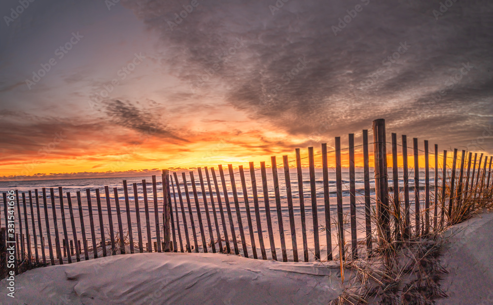 Obraz premium Sunrise at the beach with a dune fence in the foreground
