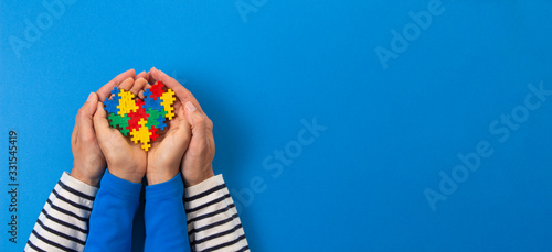 World autism awareness day concept. Adult and child hands holding puzzle heart on light blue background photo