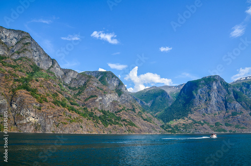 Small motor boat sails on the blue waters of the Sognefjord fjord near Flam against the background of rocky mountains and blue sky. Scandinavia  Norway