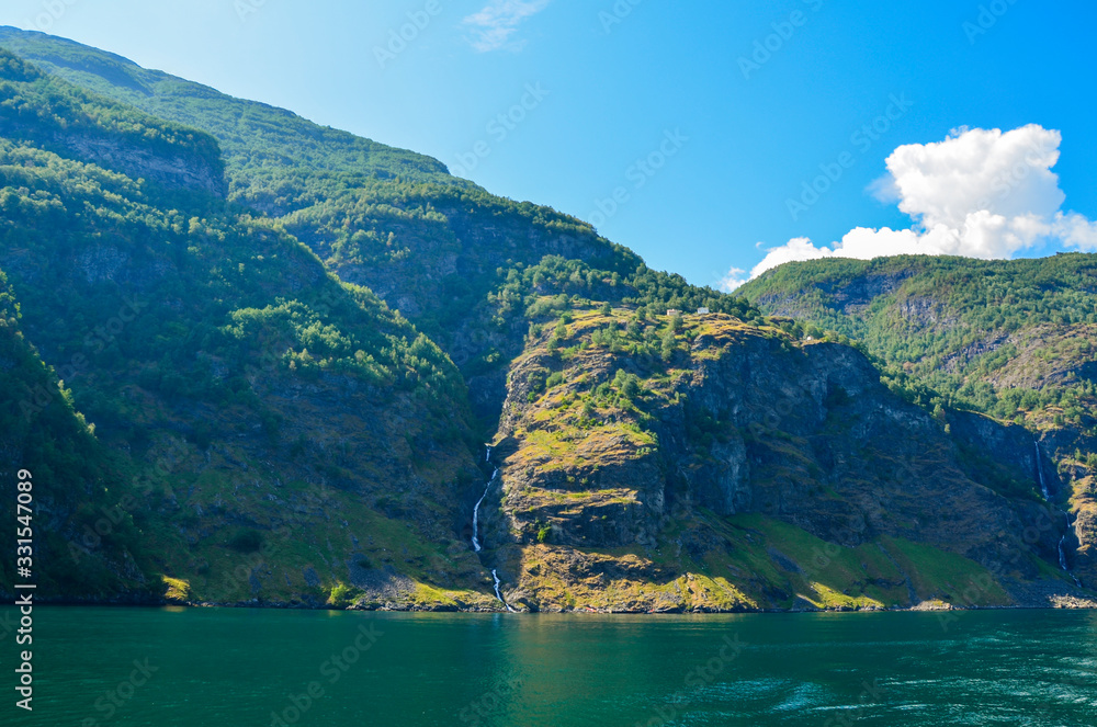 Mountains, waterfalls and various shades of the blue color of the water surface along Sognefjord,in Flam Norway, Scandinavia. Nature and travel background Mountains, waterfalls and various shades of the blue color of the water surface along Sognefjord,in Flam Norway, Scandinavia. Nature and travel background