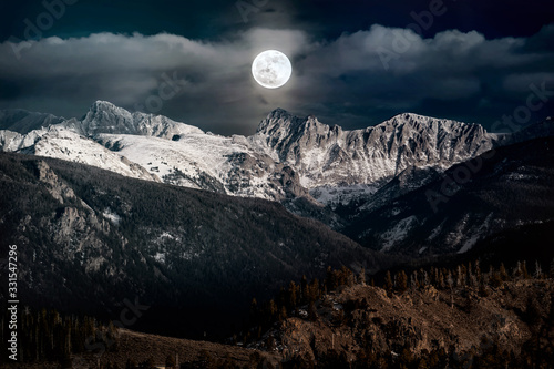 Snow peaked mountains under a full moon night sky at Rocky Mountains National Park, Colorado USA. photo