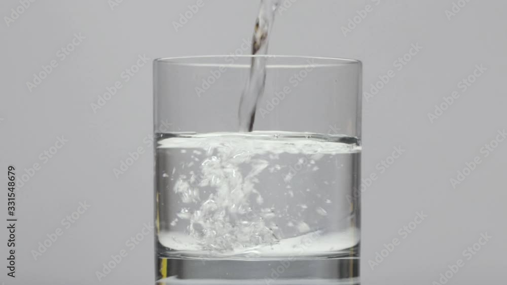 slow motion Filling a transparent glass with cold water from a glass bottle on white background slow motion Filling a transparent glass with cold water from a glass bottle on white background