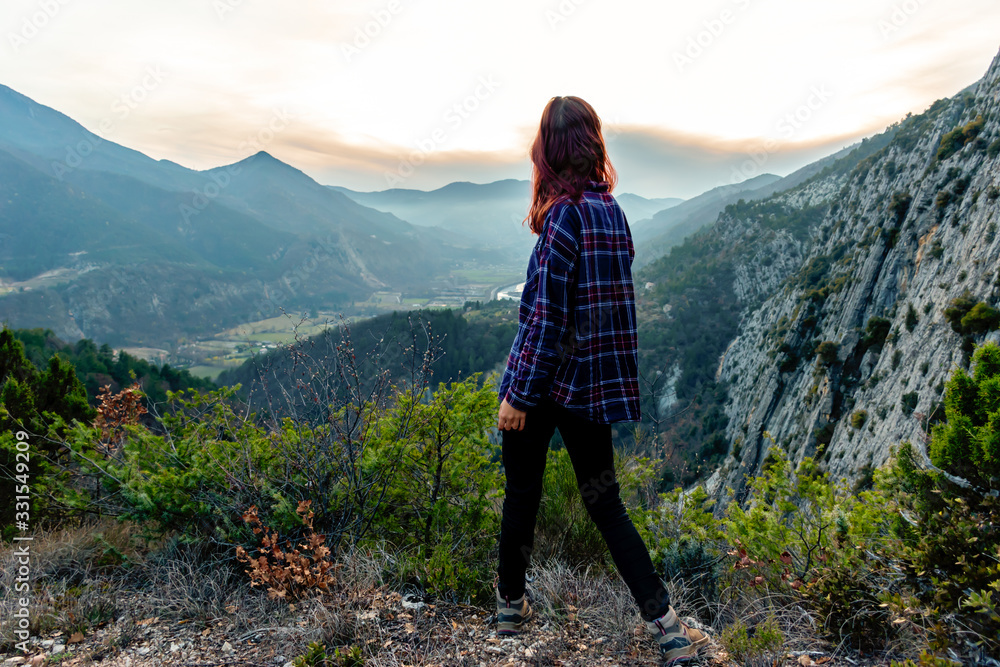 Naklejka premium A full body shot of a young female hiker / adventurer in the French Alps mountains posing during sunset