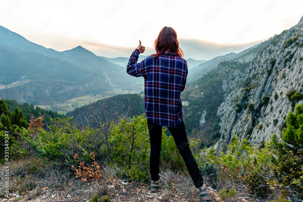A full body shot of a young female hiker / adventurer in the French Alps mountains during sunset posing with thumbs up