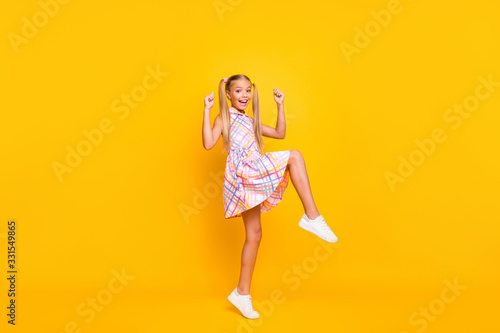 Full size profile photo of funny small lady good mood rejoicing classmates youth party raise fists leg wear checkered summer dress shoes isolated yellow bright color background