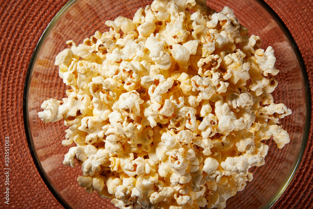 Glass bowl with salted popcorn with cheese. Heap of homemade delicious popcorn on a rustic wooden table. Snacks and food for a movie theater or cinema. Fastfood background. TV remote control Glass bowl with salted popcorn with cheese. Heap of homemade delicious popcorn on a rustic wooden table. Snacks and food for a movie theater or cinema. Fastfood background. TV remote control