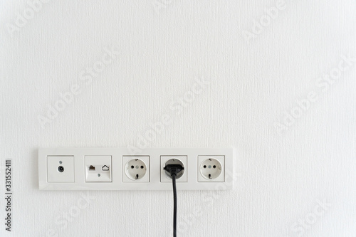 black cable cord pluged in receptacle of modern electric socket in multi paneling, internet, tv or radio adapter socket on white wall background at hom