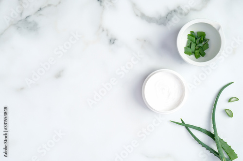 Aloe vera moisturizing cream jar and sliced plant stems on marble background. Hands dermatology and skin treatment concept. Flat lay, top view