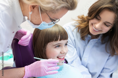 Doctor examining child teeth with instrument and mirror. Mother controlling process. 
