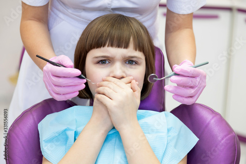 Screaming little patient with covered mouth by hand sitting on chair at dental office. 