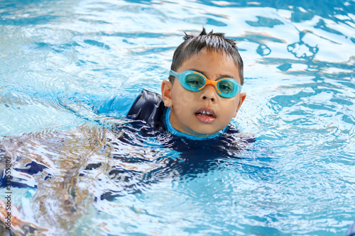 Happy child playing in blue colour swimming pool. Boy with swimming goggles. Kid practice water sport. Summer vacation concept.
