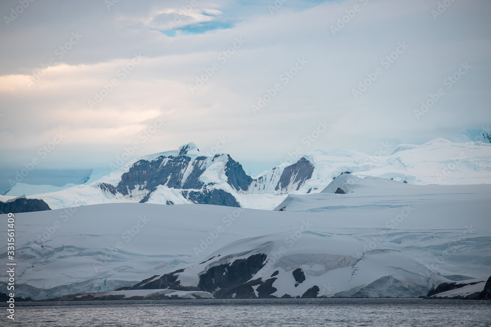 Obraz premium glacier in the mountains coastline of antarctica with rocks and snow at the sea with clouds 