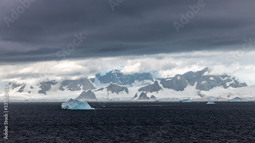 glacier in the mountains coastline of antarctica with rocks and snow at the sea with clouds and iceberg 