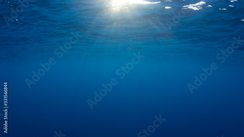Underwater background with sunburst on surface of clear blue ocean 
