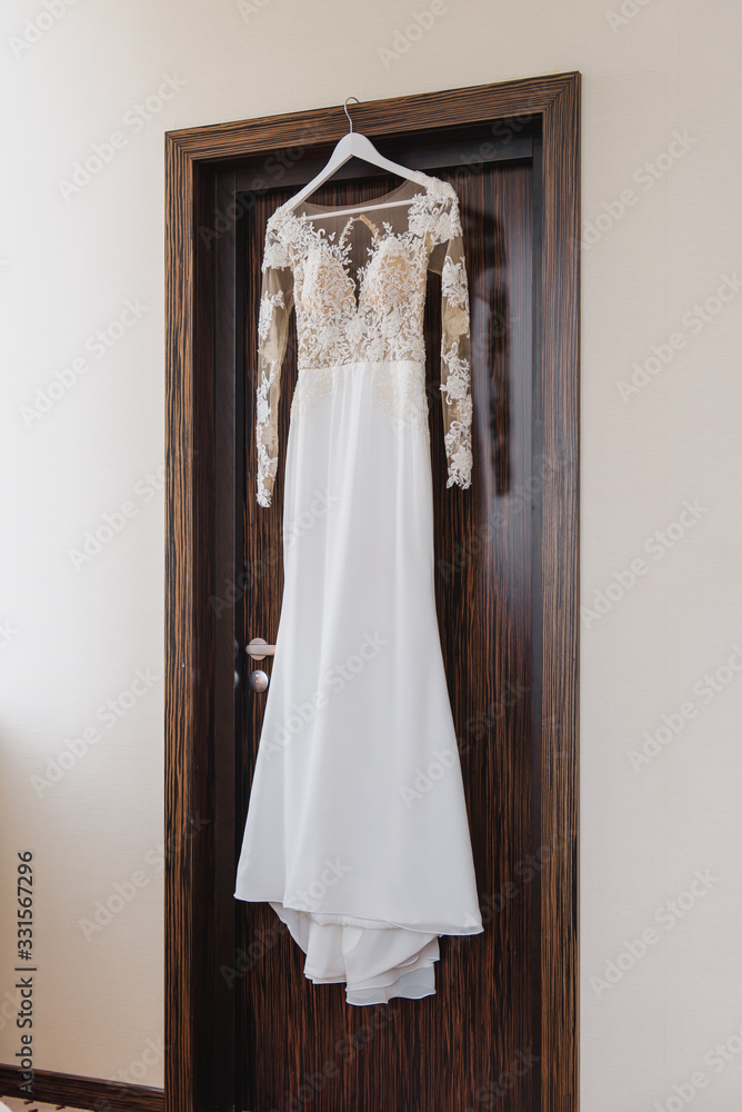 Elegant wedding white dress hanging on a wooden door during a wedding preparation. Bride's morning. Before ceremony Elegant wedding white dress hanging on a wooden door during a wedding preparation. Bride's morning. Before ceremony