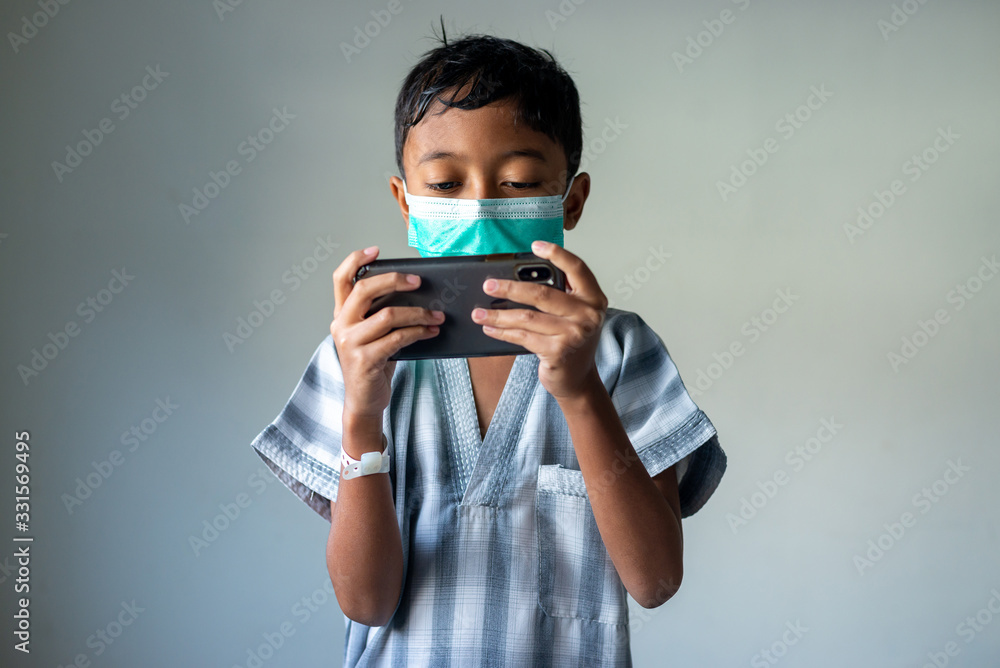 Young Muslim Boy wearing a mask playing games on the smartphone. Covid-19 coronavirus concept. Shallow depth of field. Young Muslim Boy wearing a mask playing games on the smartphone. Covid-19 coronavirus concept. Shallow depth of field.