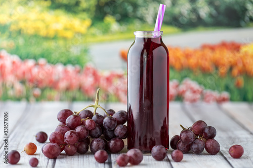 Fotografia A close up view of a glass bottle of grape juice surrounded by grapes against a garden background