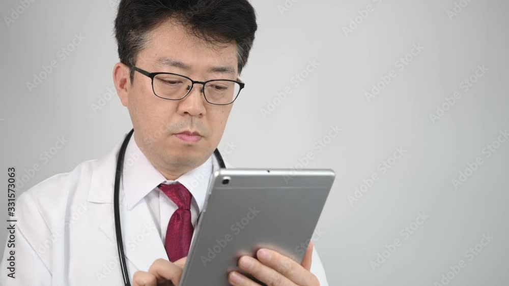 4K. Middle-aged Asian male doctor who uses a tablet computer to take telemedicine. 4K. Middle-aged Asian male doctor who uses a tablet computer to take telemedicine.